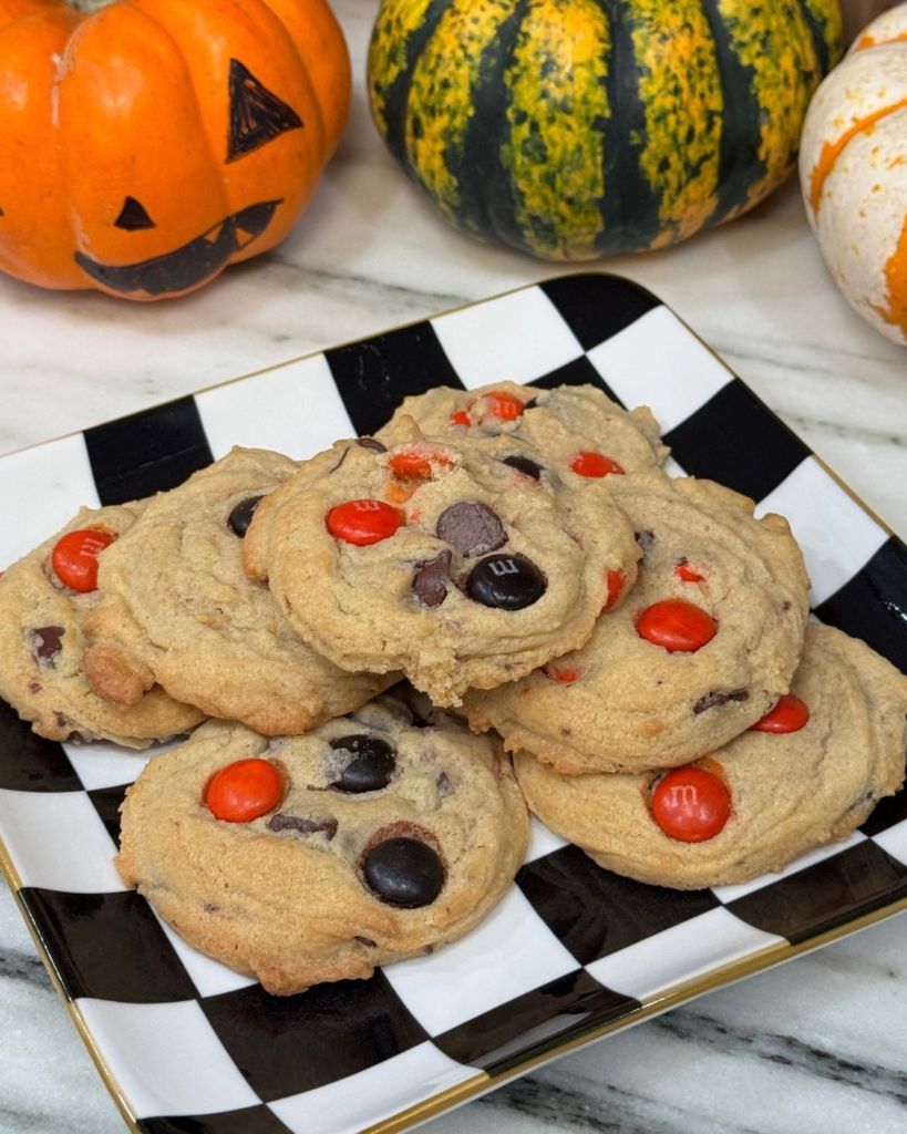 Stack of chocolate chip M&M cookies with orange candies and chocolate chips on a black-and-white checkered plate.