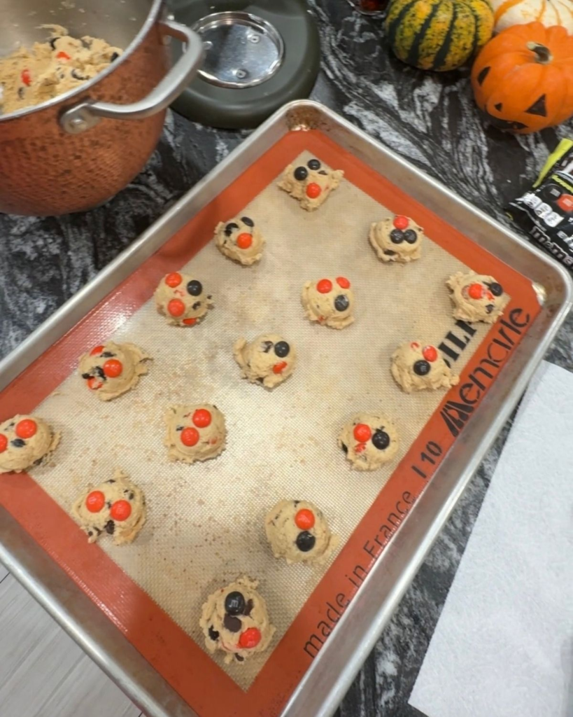 Scoops of M&M cookie dough topped with extra candies and chocolate chips before baking.