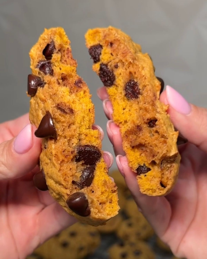 Soft pumpkin chocolate chip cookie broken in half showing the fluffy pumpkin center and chocolate chips