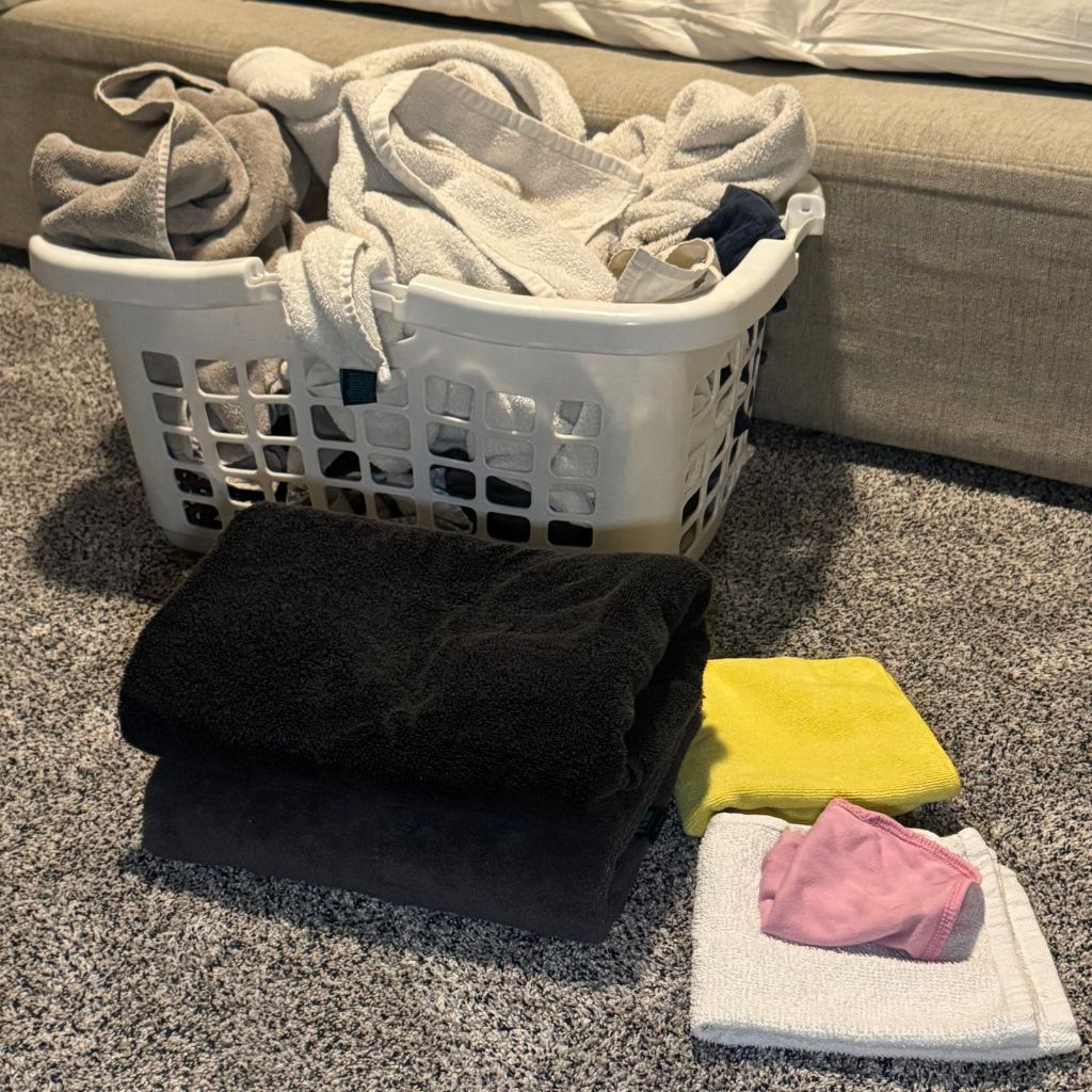 Folded laundry and towels on the floor during a realistic day in the life of a mom of two