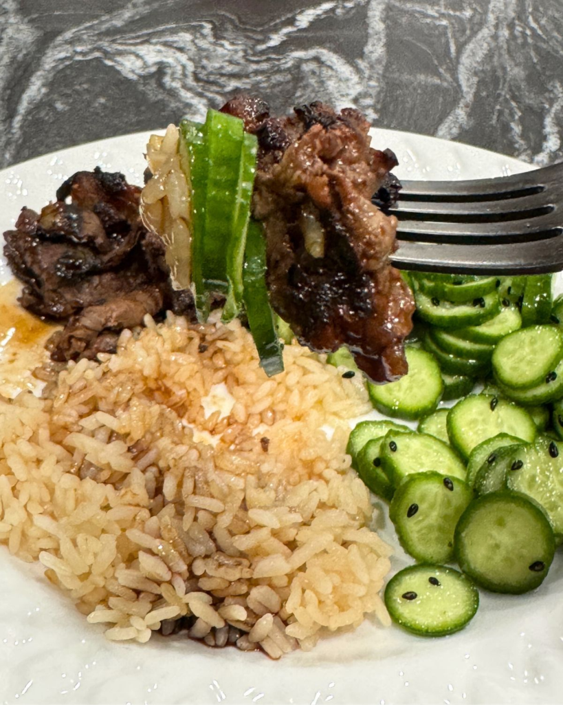 Fork bite of Costco shabu shabu beef with rice and cucumber salad.