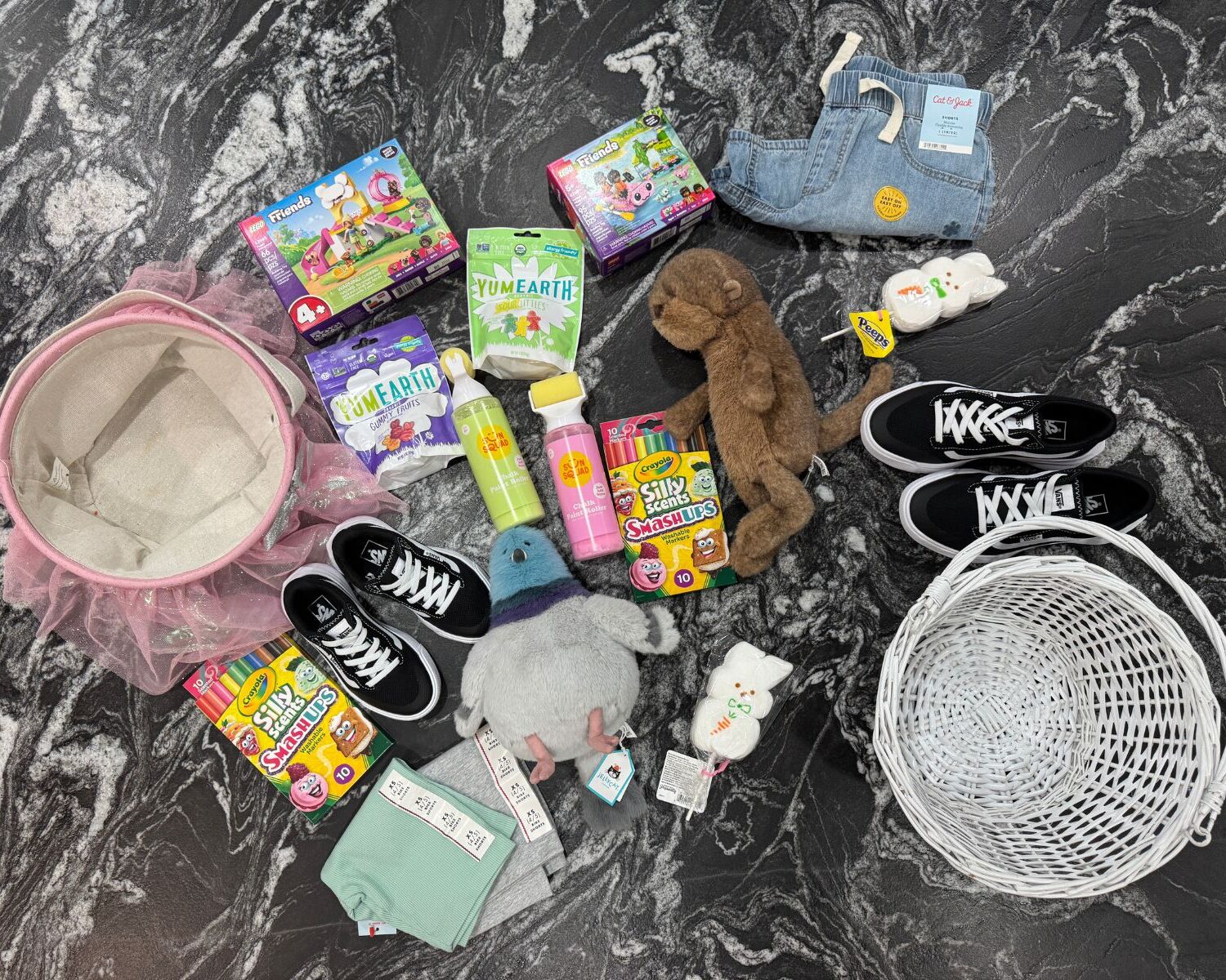 Flat lay of Easter basket ideas for girls including plush toys, LEGO sets, candy, crayons, shoes, and spring clothing.