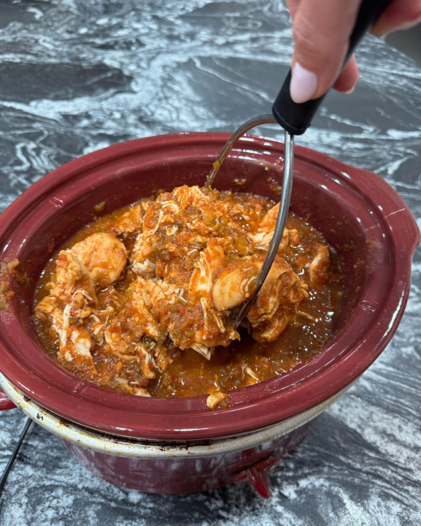 shredding salsa chicken in a crockpot with a meat shredder tool
