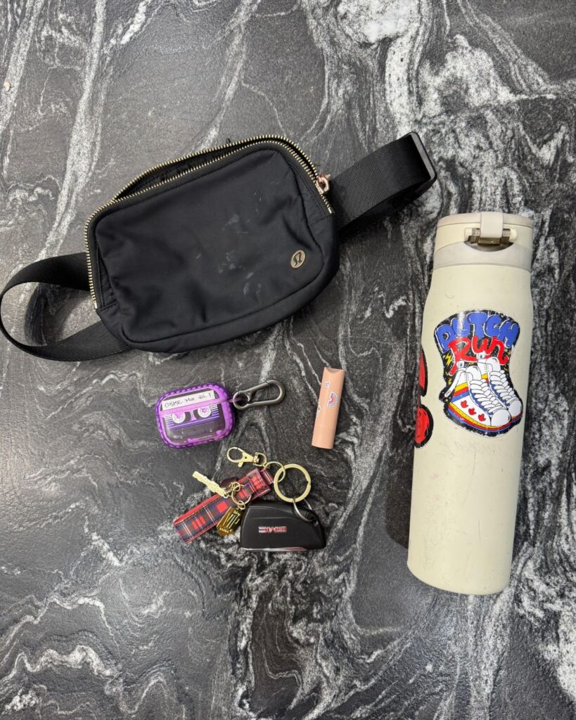 Belt bag, keys, lip balm, AirPods case, and water bottle for simple gym bag essentials as a busy mom