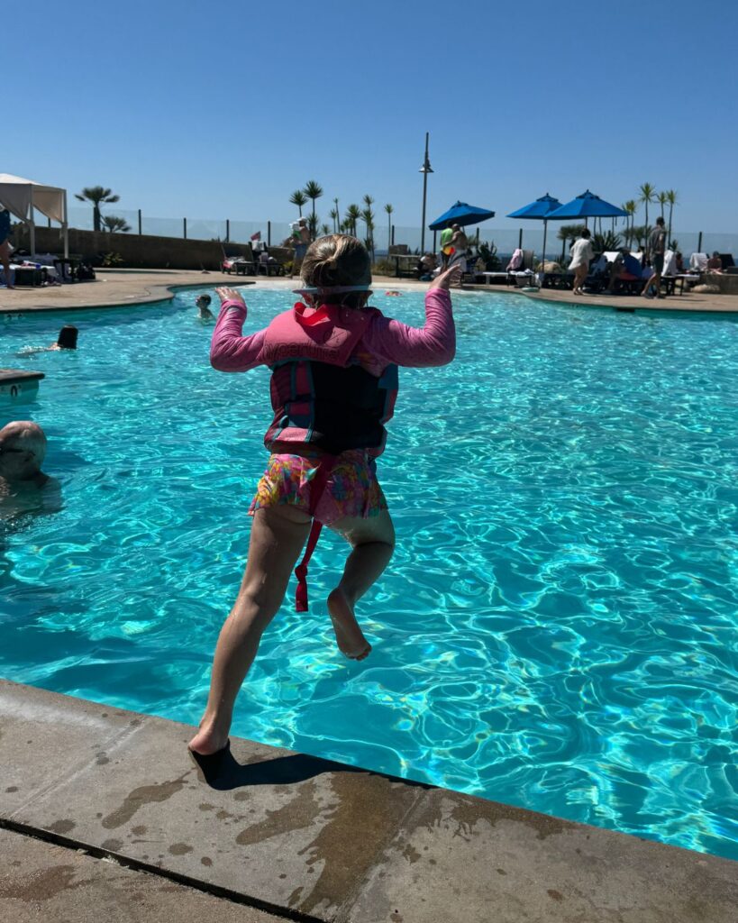 Young girl jumping into the resort pool during a family trip to Carlsbad California