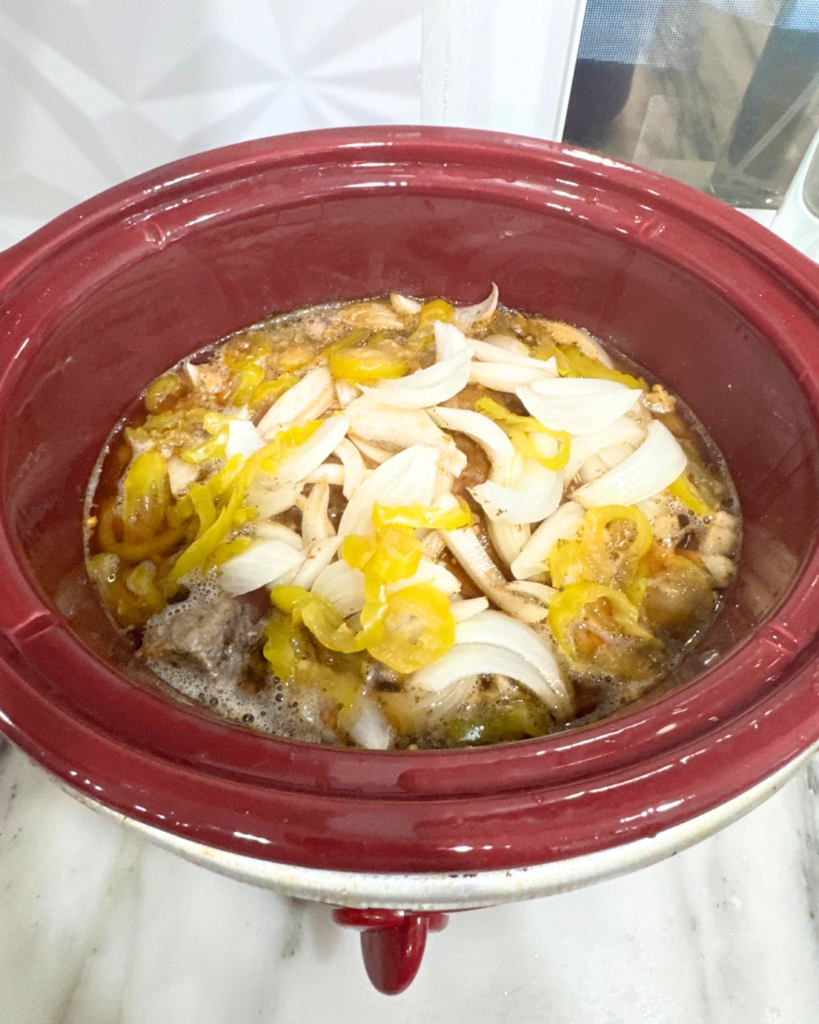 Birria beef cooking in broth in slow cooker before shredding