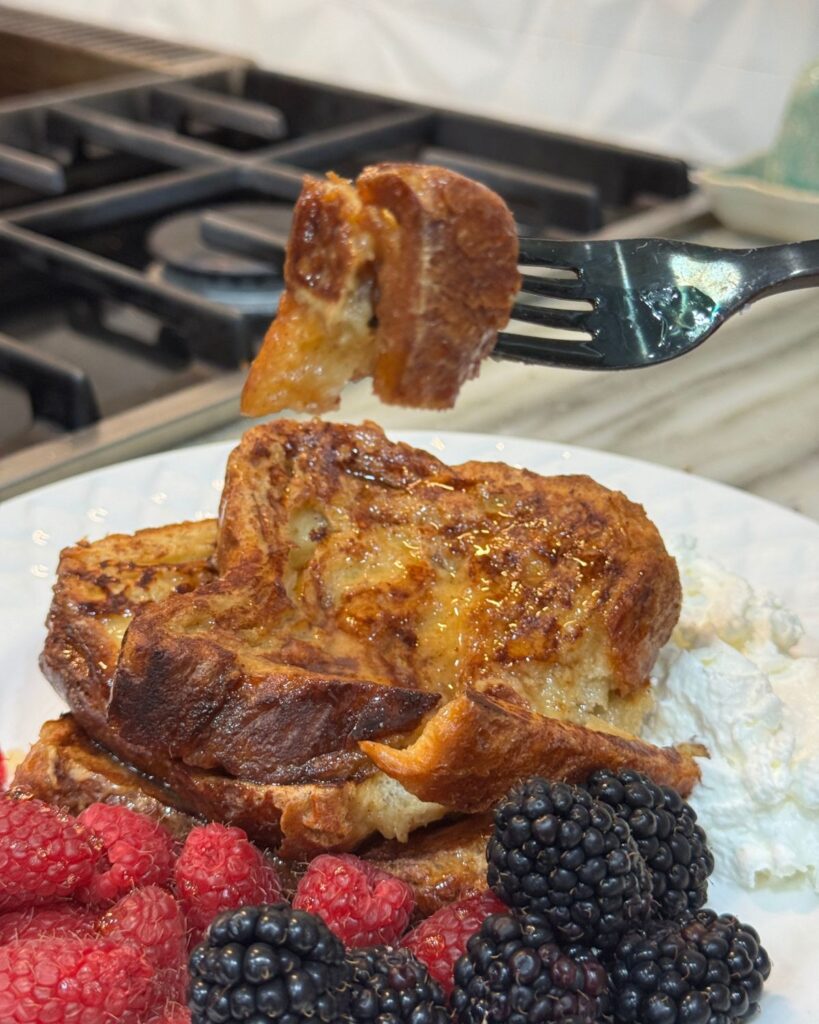 Fork holding a bite of croissant French toast showing the soft custardy texture