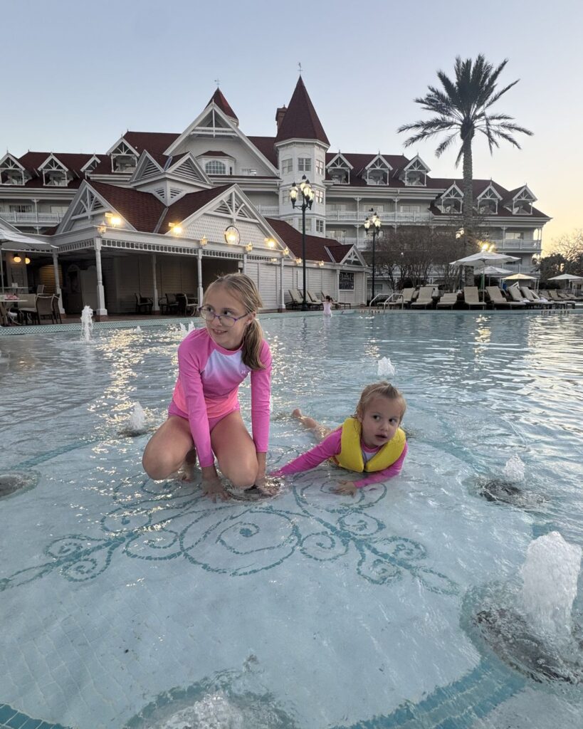 Two girls playing in a Disney resort pool wearing rash guards and a life jacket.