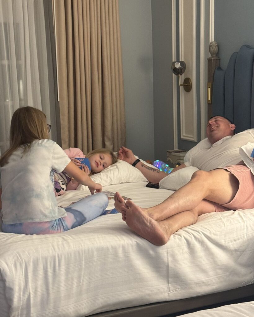 Kids and dad playing cards together on a Disney resort hotel bed after park day.