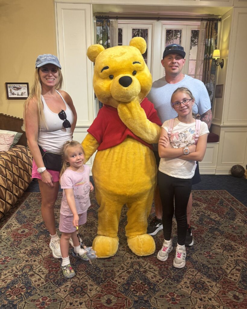 Family meeting Winnie the Pooh at Disney World wearing belt bags, hats, and sunglasses.