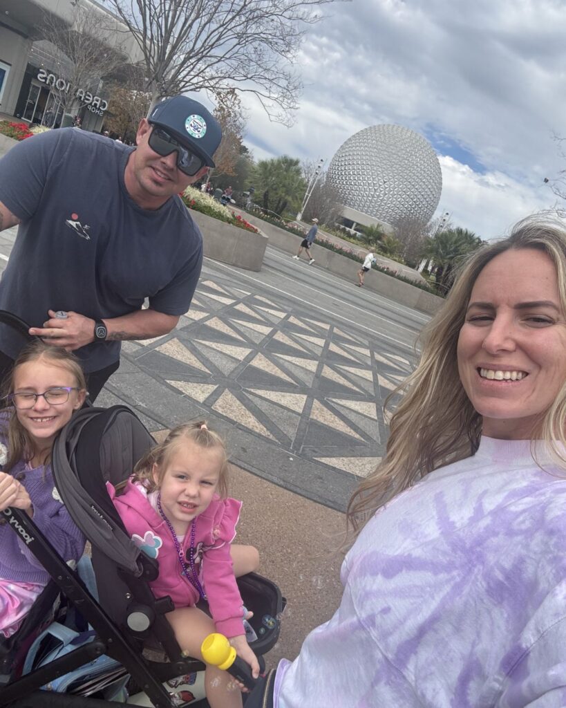 Dad pushing stroller with two kids at EPCOT with Mom and Spaceship Earth in the background.
