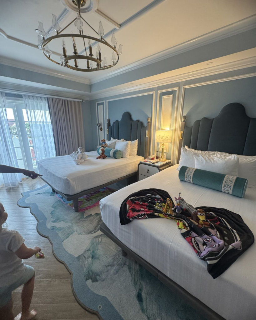 Disney resort hotel room with two beds and kids’ stuffed animals and park gear.