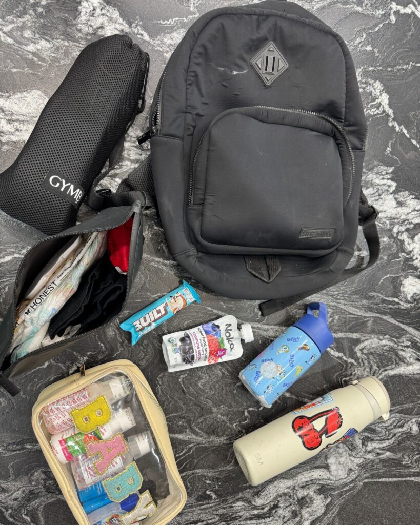 Simple flat lay of a gym bag, toddler supplies, toiletries, snacks, and water bottles for busy mom workouts