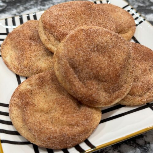 Homemade snickerdoodle cookies stacked on a striped plate