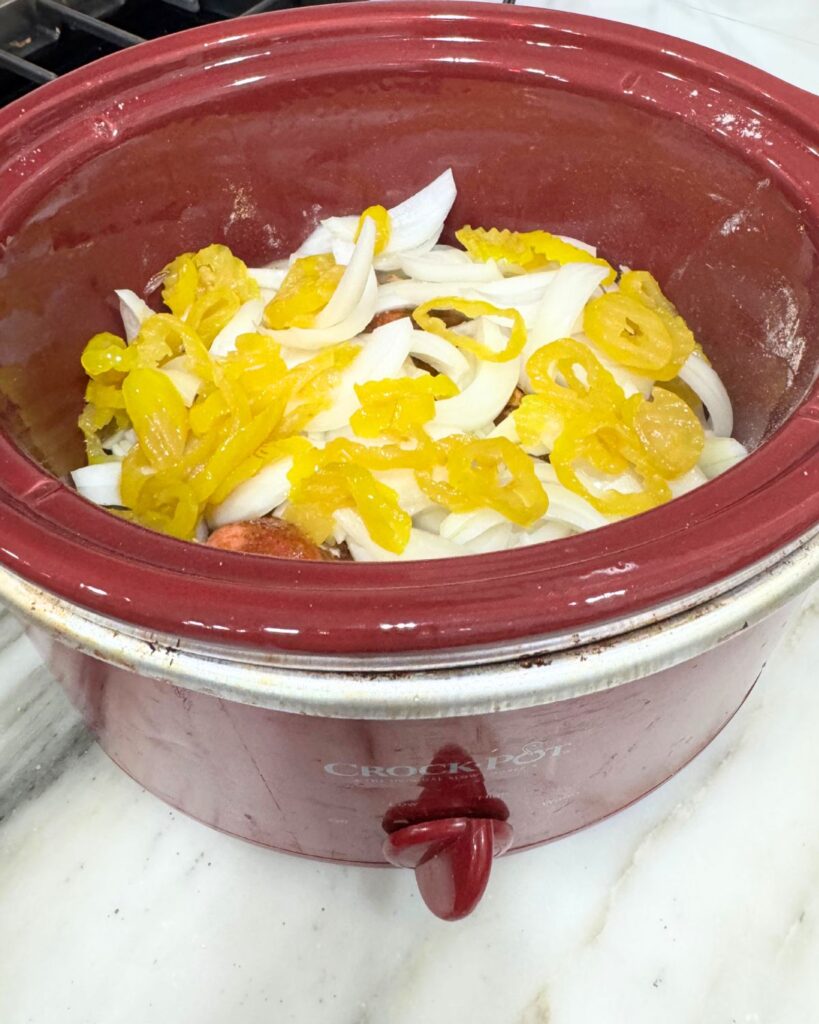 Onions and pepperoncini added to crockpot for slow cooker birria
