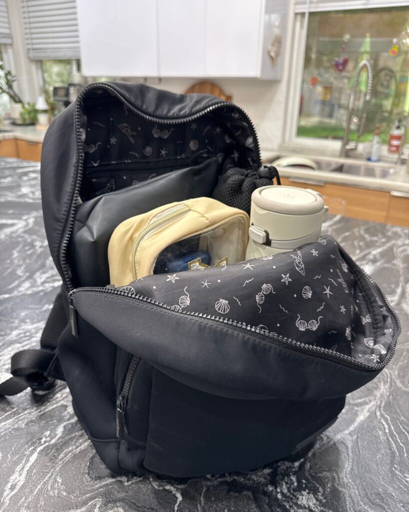 Packed black gym bag open on a kitchen counter with pouches, water bottle, and busy mom gym essentials