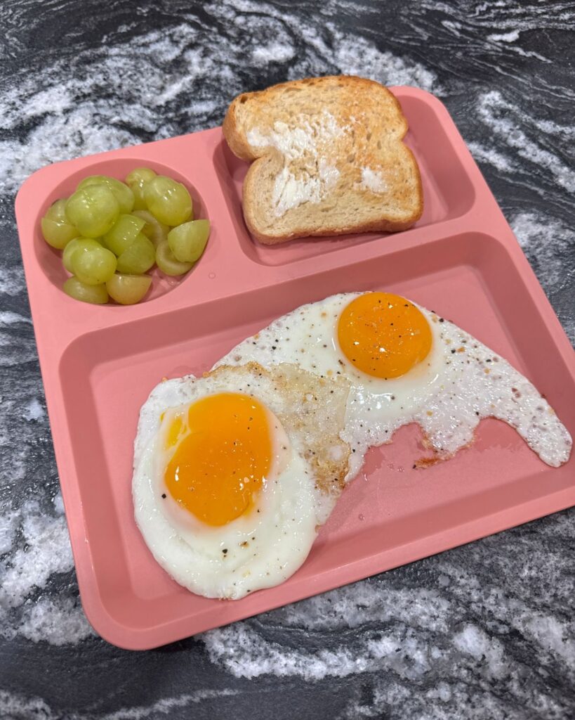 Fried eggs with toast and grapes served on a pink divided plate for an easy high protein breakfast