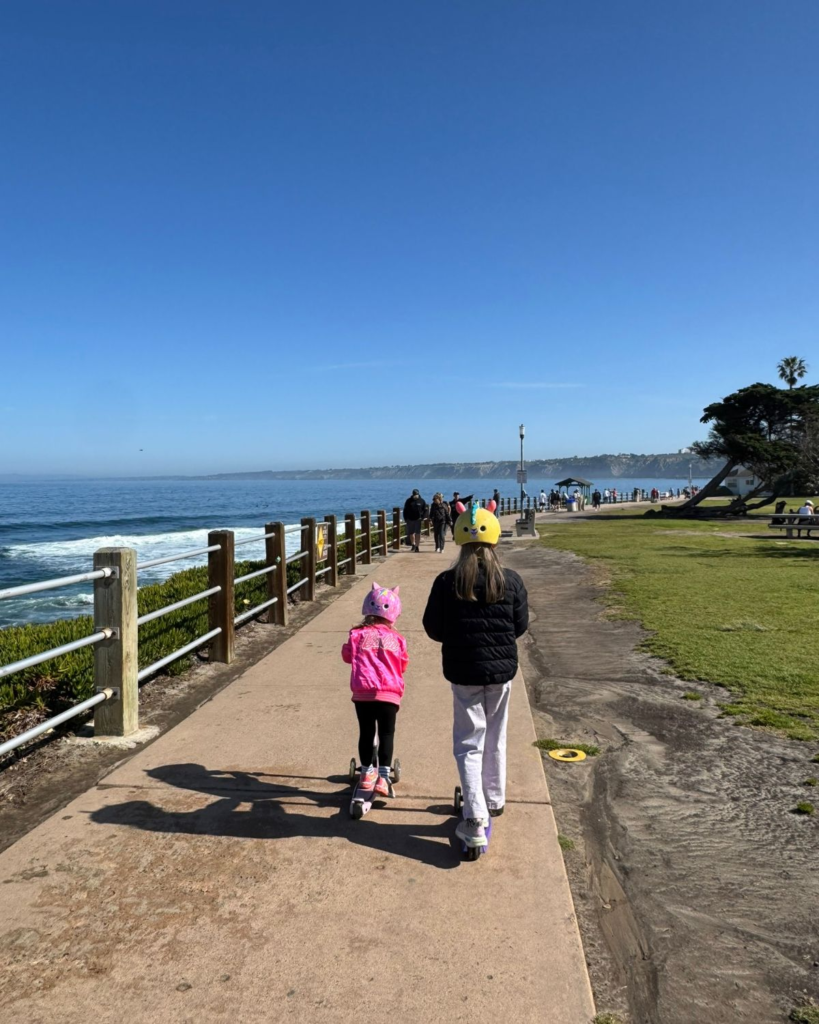 Two young girls riding scooters along the coastal walkway in La Jolla.