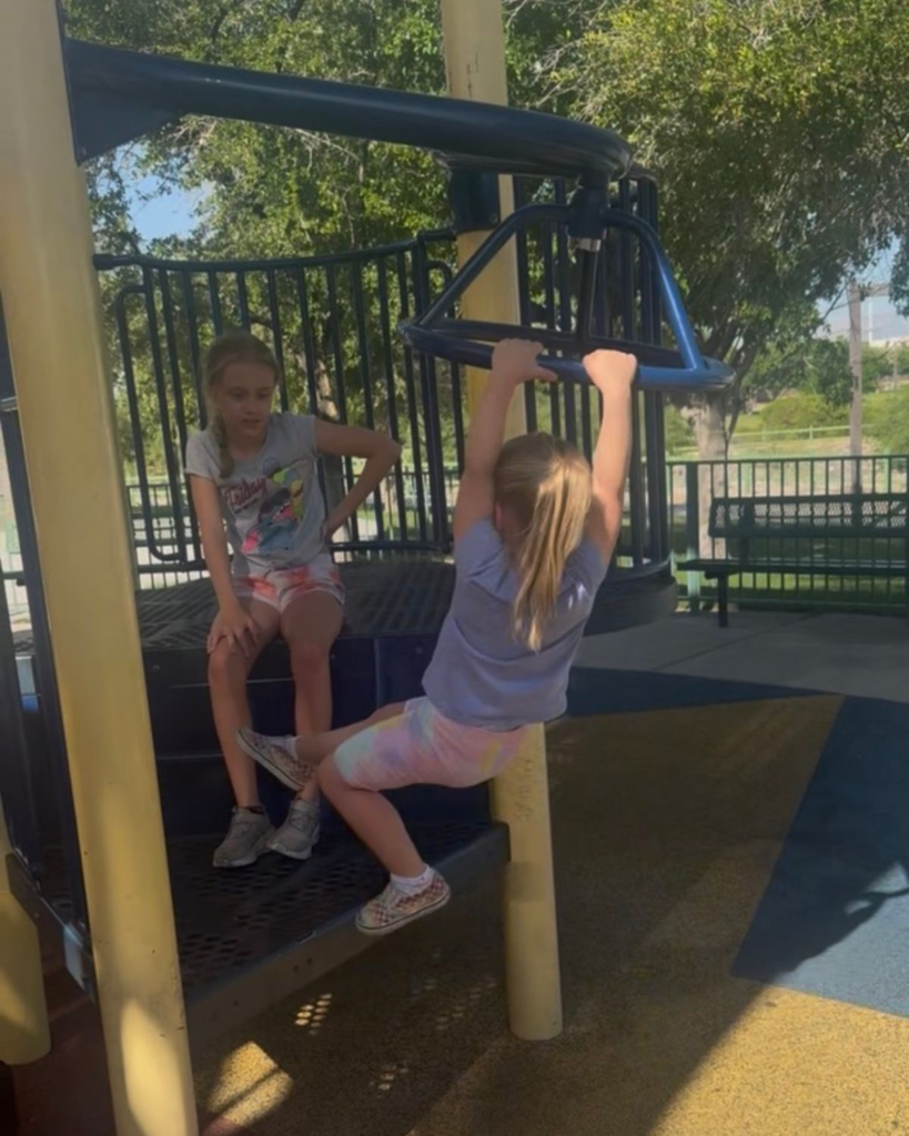 Two young girls playing together at a neighborhood playground during summer break.