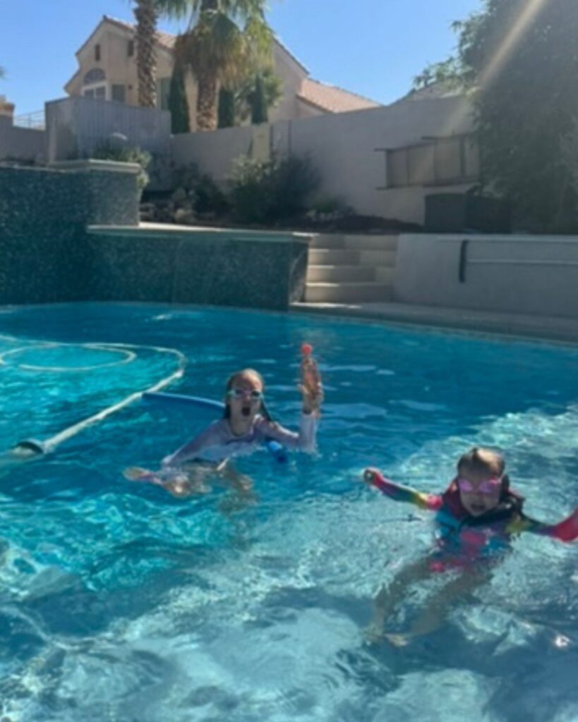 Two girls swimming in a backyard pool on a sunny summer day during a realistic summer routine for busy moms.