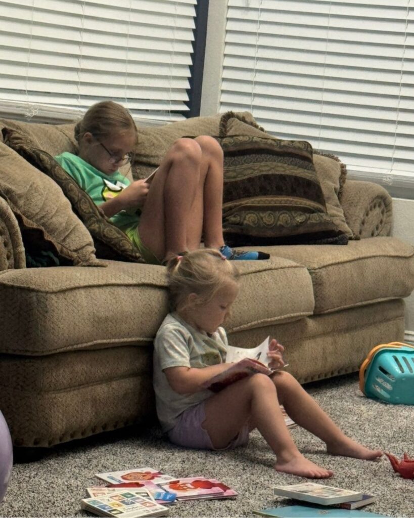 Two sisters reading books quietly in the living room during afternoon quiet time at home.