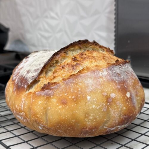 Freshly baked homemade sourdough bread with a golden crust cooling on a wire rack.