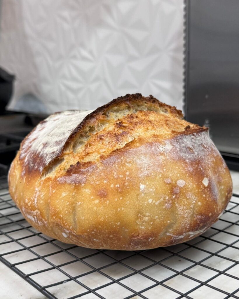 Freshly baked homemade sourdough bread with a golden crust cooling on a wire rack.
