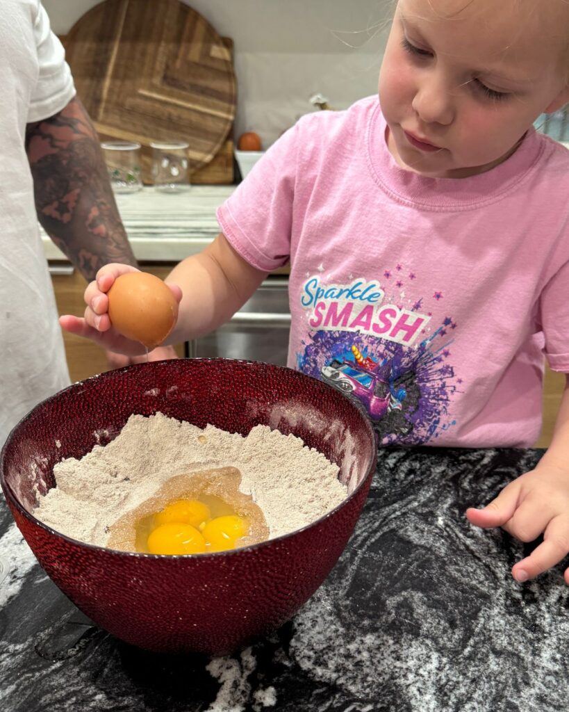 Young girl cracking eggs into a bowl while helping make homemade protein pancakes.