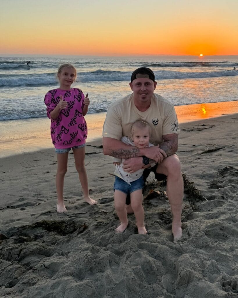 dad with daughers on pacific beach at sunset with surfers in the background