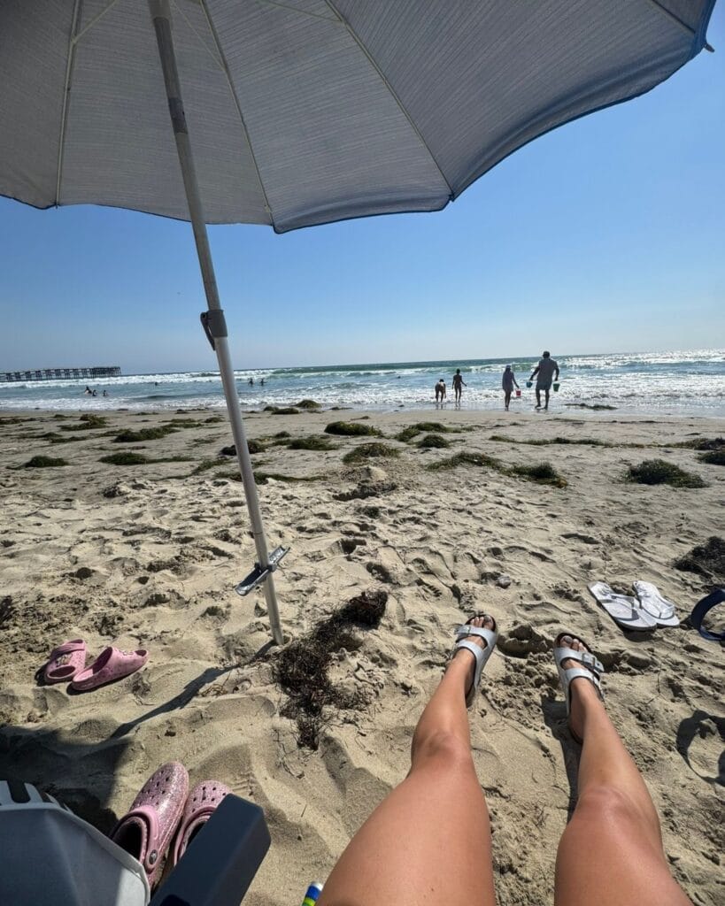 mom sitting in beach chair under beach umbrella watching kids play in sand with beach toys provided by pacific terrace hotel in pacific beach