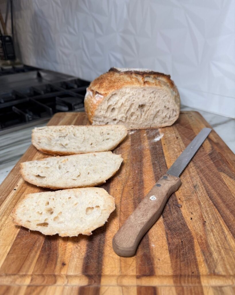 Sliced homemade sourdough bread on a wooden cutting board with a bread knife.