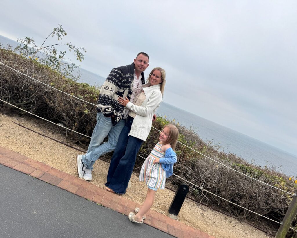 Mom, dad and daughter standing on pathway overlooking ocean after dinner.