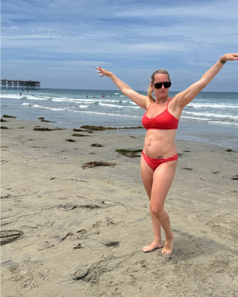 Julie on the beach in 2026 before her breast lift and implant exchange surgery.