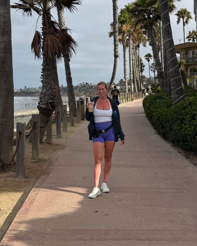 Julie walking along a palm tree-lined beach path before her breast lift and implant exchange.