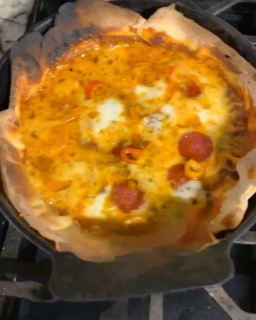 Homemade sourdough pizza dough baking in a cast iron skillet with mozzarella cheese, pepperoni, and peppers.