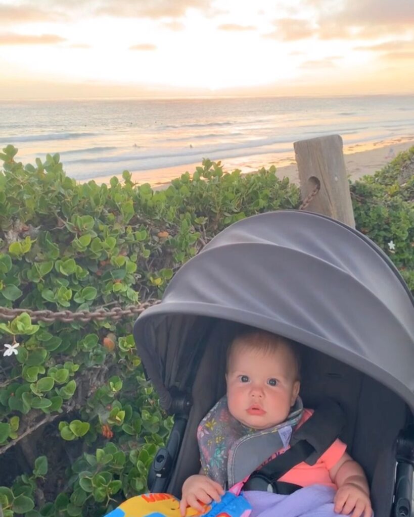 Baby in a stroller on the boardwalk overlooking the beach outside Pacific Terrace Hotel at sunset.