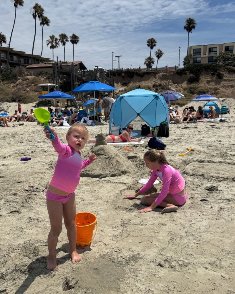 Kids playing in the sand with Pacific Terrace Hotel overlooking the beach behind them.
