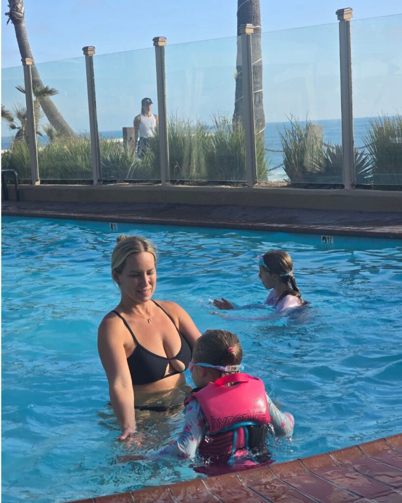 Mom swimming with her daughters in the oceanfront pool at Pacific Terrace Hotel.