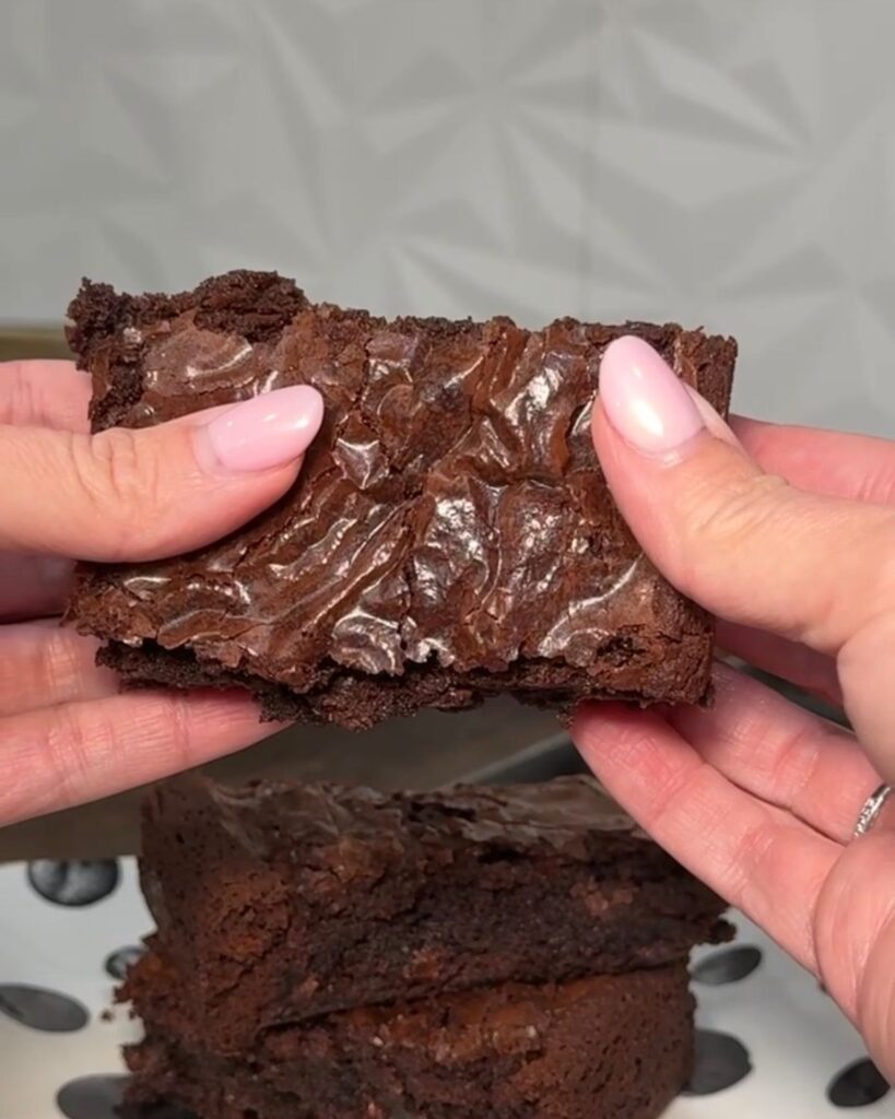 Thick homemade brownie with a crackly top and fudgy center held in both hands.
