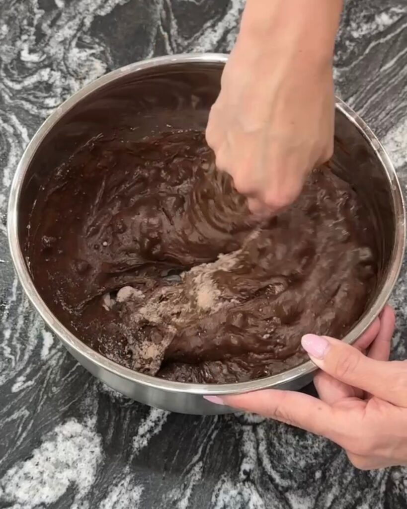 Mixing thick brownie batter together in a large bowl with a whisk.