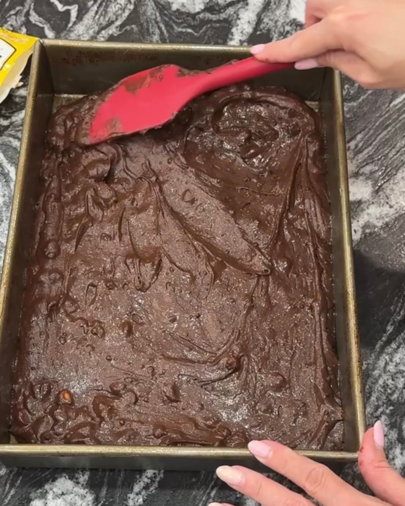 Thick chocolate brownie batter spread evenly into a greased 9x13 baking pan.