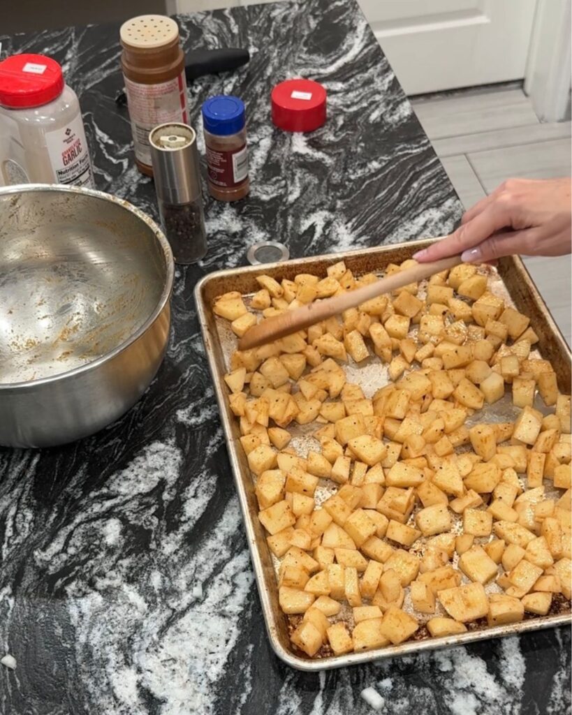 Seasoned diced potatoes spread on a baking sheet before roasting for cheesesteak bowls