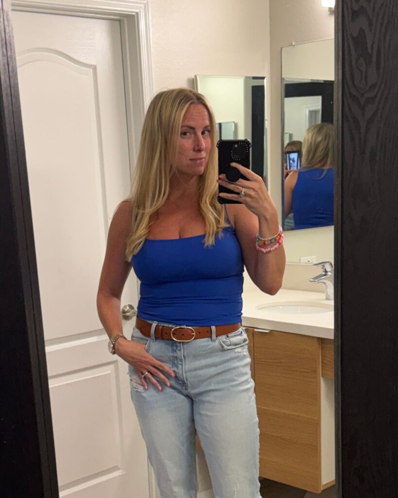 Woman before a breast lift and implant exchange wearing a blue tank top and jeans