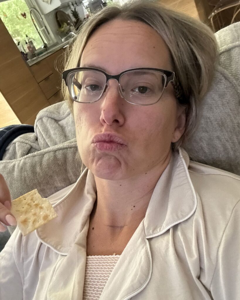Julie resting at home after breast lift and implant exchange surgery while eating a saltine cracker