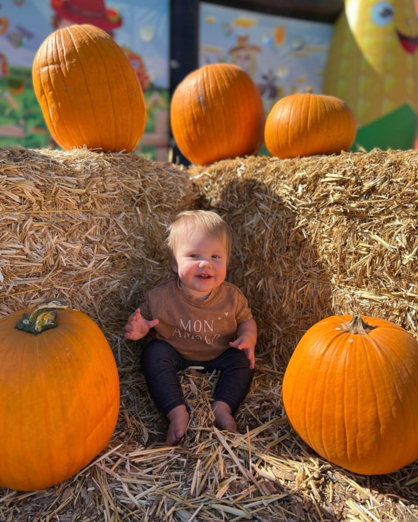 Young girl sitting in hay surrounded by pumpkins at a fall pumpkin patch