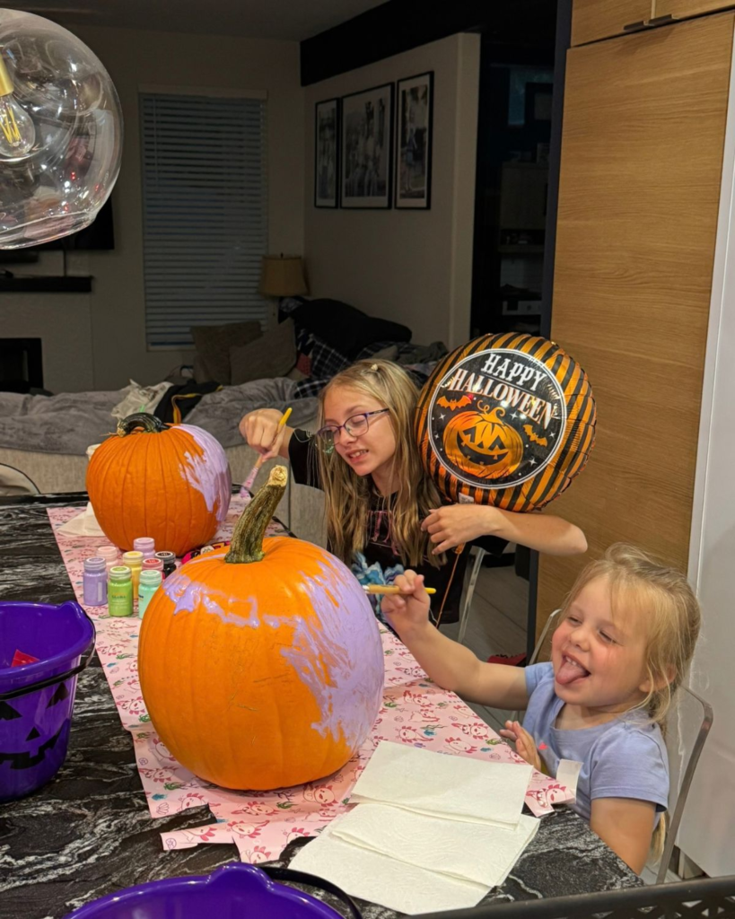 Two girls decorating pumpkins with paint at home for Halloween
