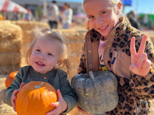 Two sisters posing together with pumpkins at a fall pumpkin patch