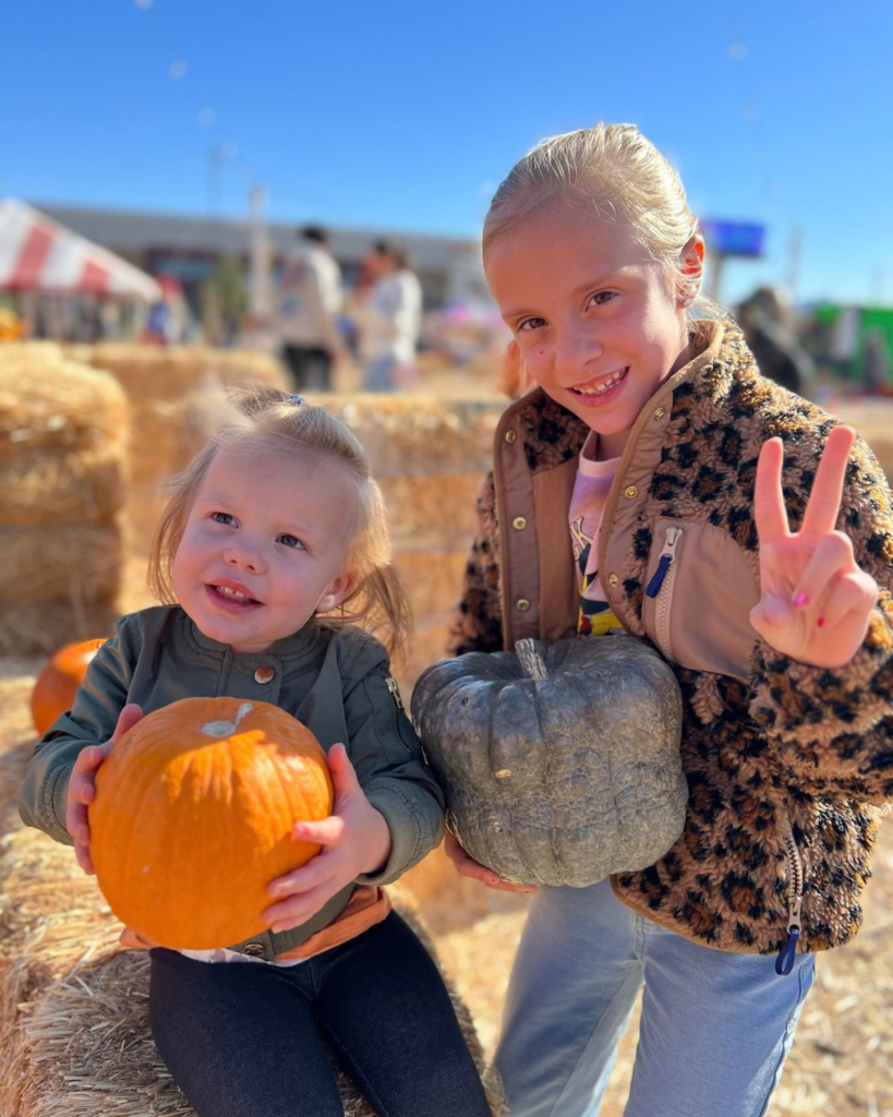 Two sisters posing together with pumpkins at a fall pumpkin patch