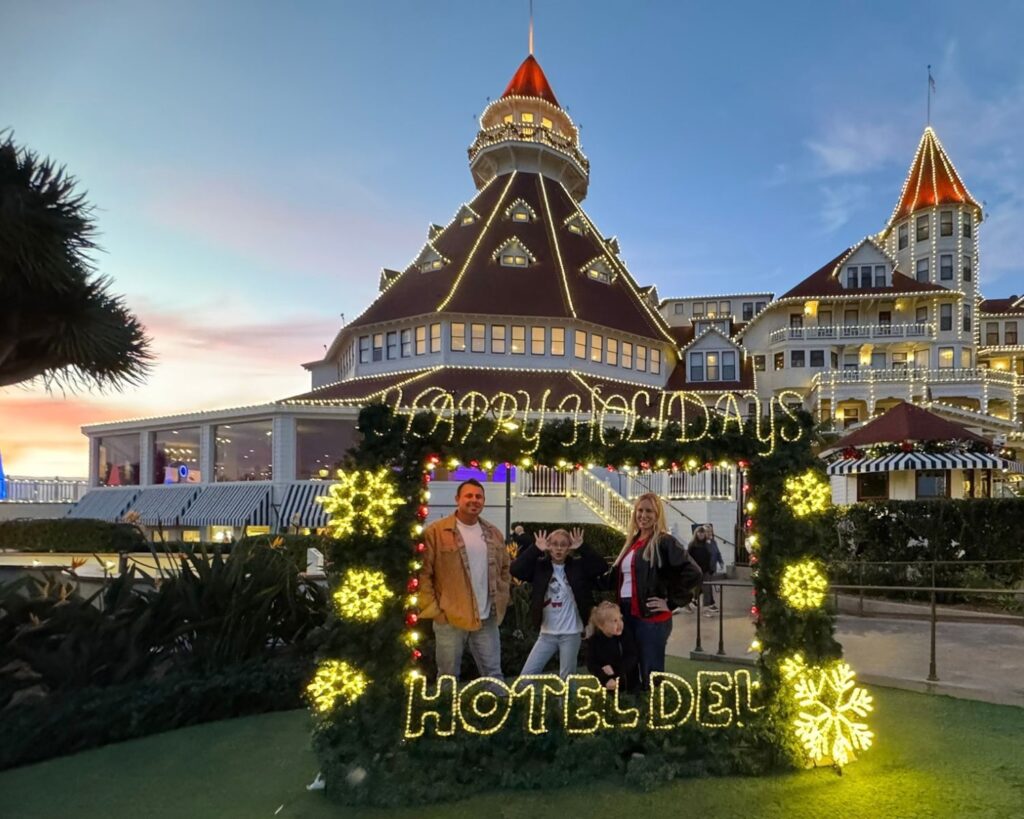 Family posing outside Hotel Del Coronado at sunset with the hotel illuminated behind them