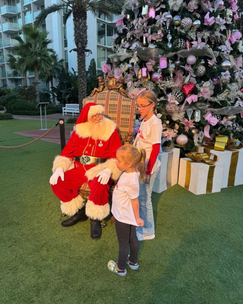 Two young girls visiting Santa Claus beside a decorated Christmas tree